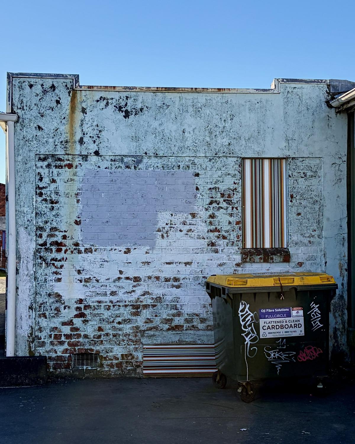 300 West laneway, both strips in place: the upright Strip Painting in the boarded window of the mint brick gable, and a low strip at the foot of the wall